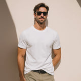 Man wearing a white t-shirt and sunglasses against a beige wall