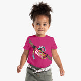 A young girl wearing a pink short-sleeved crew neck t-shirt with character and text graphics, paired with light-colored shorts and a wide belt.