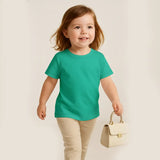 Child wearing a green shirt and beige pants, holding a small cream-colored handbag on a plain background