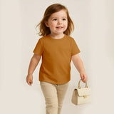 Child wearing a mustard yellow shirt and beige pants, holding a small cream handbag on a plain background