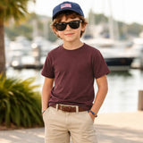 Child wearing burgundy tee, sunglasses and a cap by a waterfront